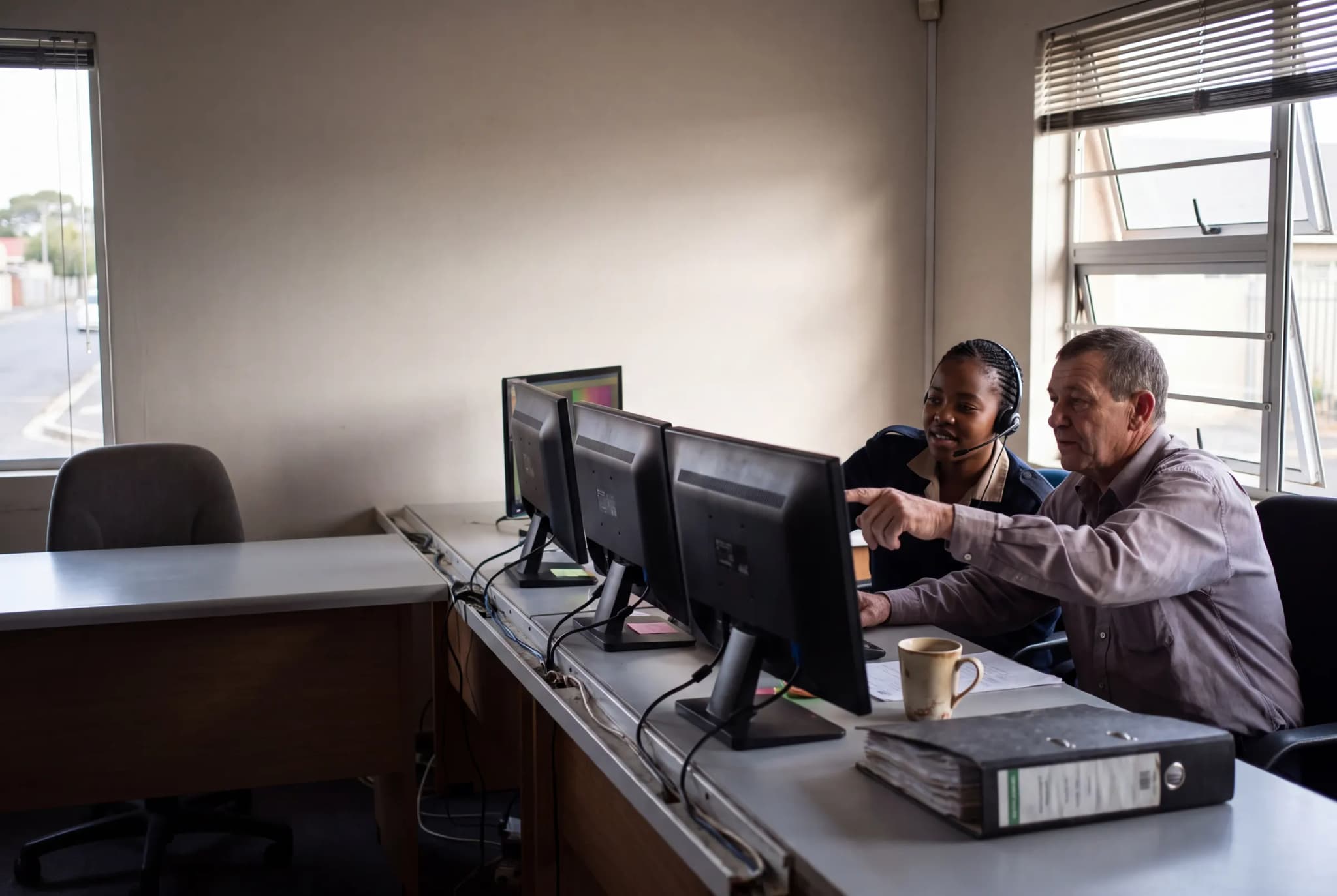 Two control-room operators at a desk of monitors, working through the morning